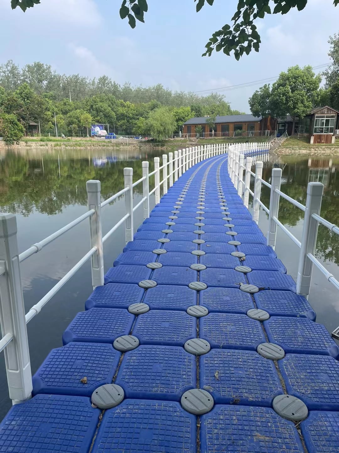 Curved blue modular floating bridge with white railings over a landscaped pond