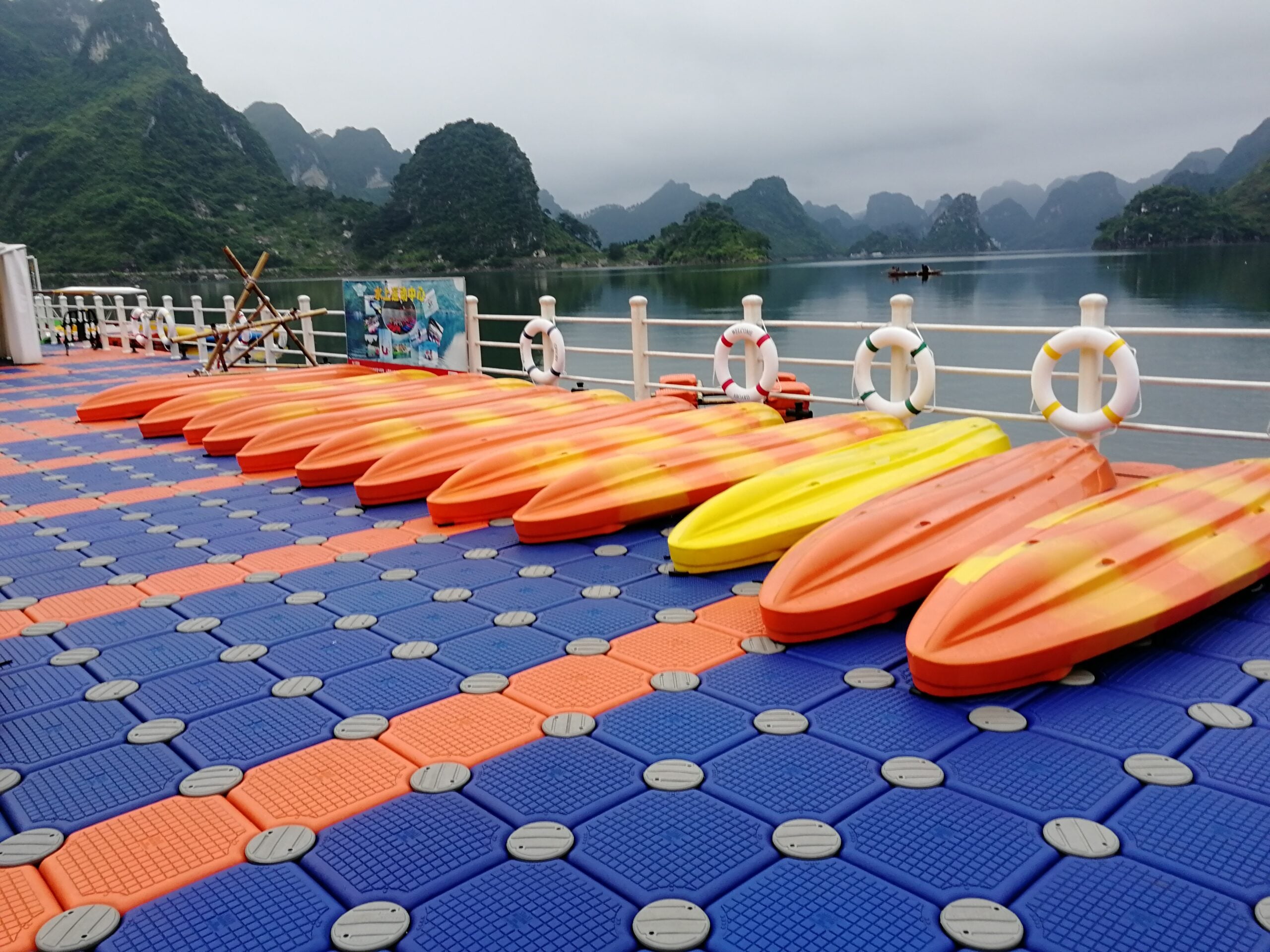 Blue and orange modular platform with rows of kayaks beside a lake