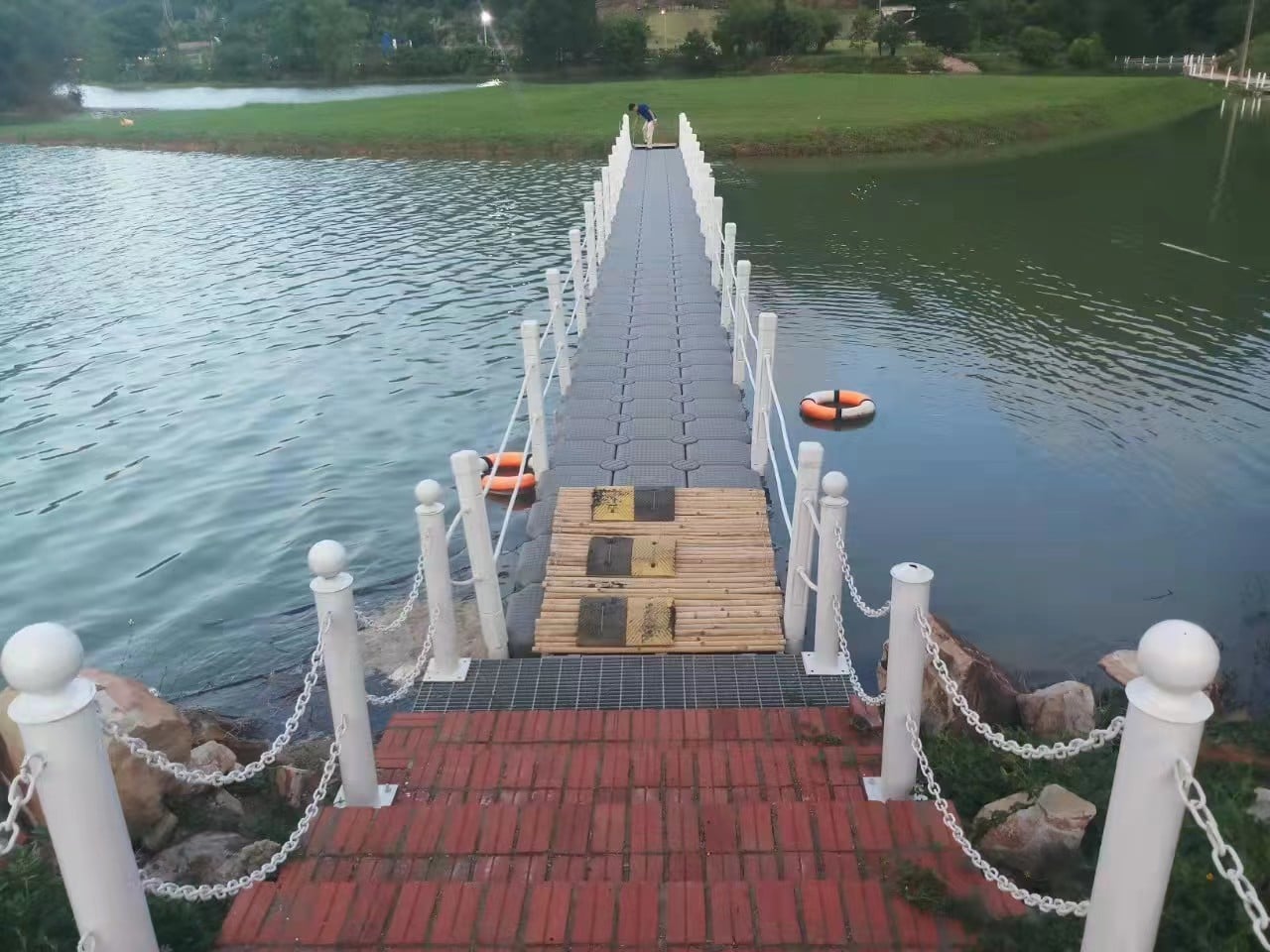 Grey floating bridge joined to a shore transition, with lifebuoys alongside