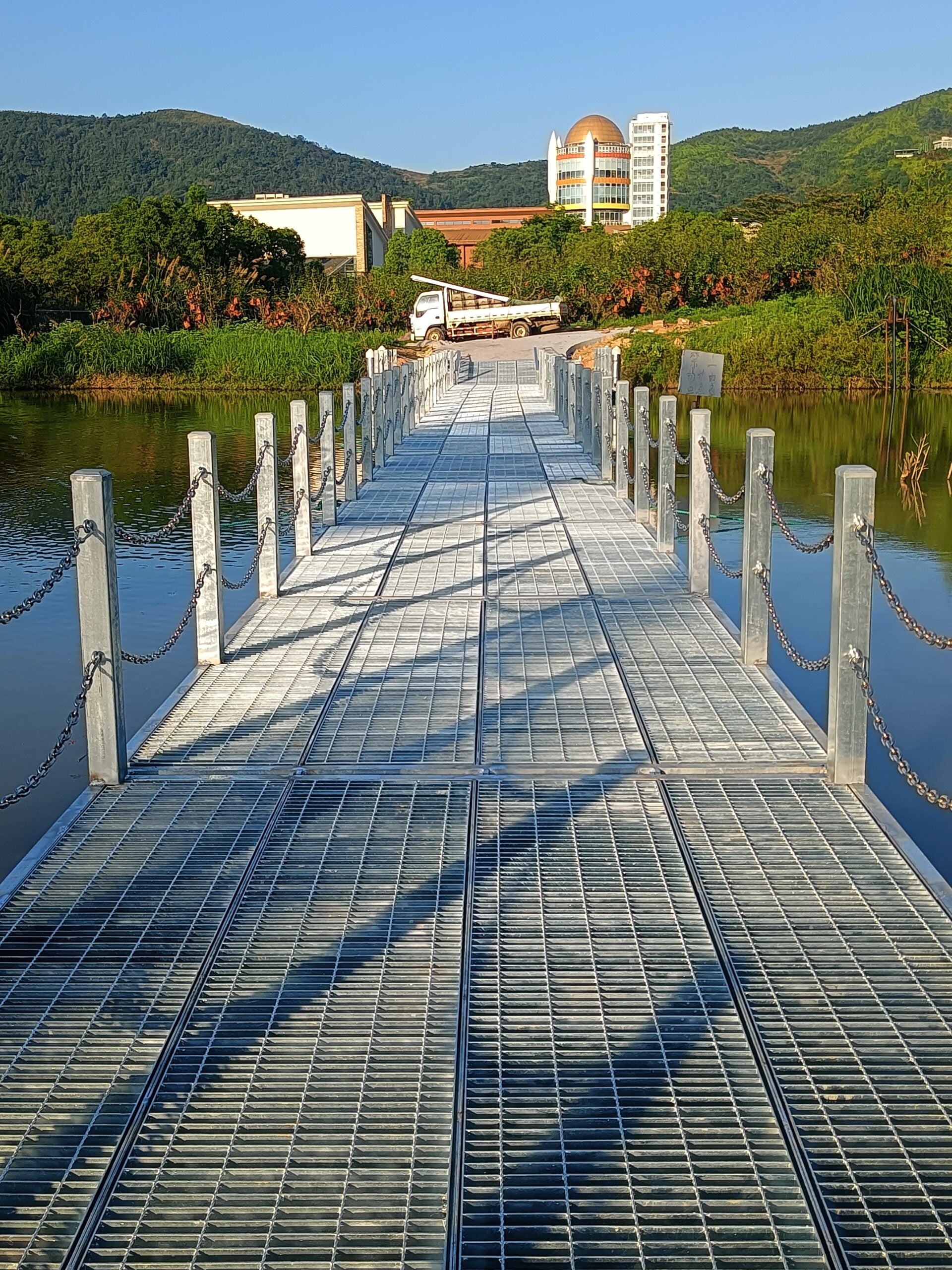 Metal-grating walkway approaching the shore with posts and chains